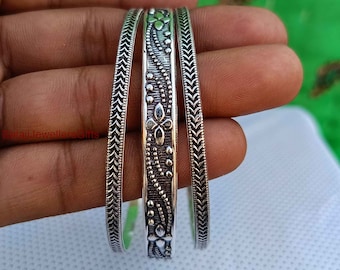 May include: Three silver bangles with intricate designs. The bangles are stacked on top of each other and have a textured finish.