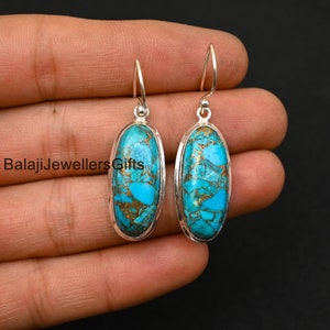 Puede incluir: Un par de pendientes colgantes de plata con piedras ovaladas de turquesa. Las piedras tienen un patrón de mármol azul y dorado.
