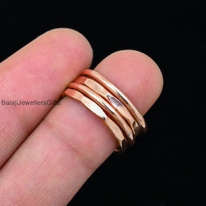 Puede incluir: Conjunto de cuatro anillos apilables de oro rosa martillado. Los anillos se llevan en un dedo y están hechos de un metal liso y brillante.