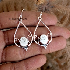 May include: Silver teardrop earrings with a white spiral design. The earrings have a delicate, openwork design with a small cluster of beads at the bottom. The text "BalajiJewellersGifts" is visible.