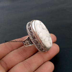 May include: A silver ring with a large, oval white stone with grey veining. The ring has an ornate, filigree design around the stone and on the band. The text "BalajiJewellersGifts" is visible on the ring.