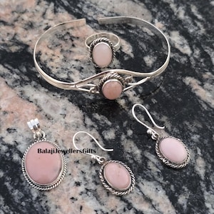Peut inclure: Un ensemble de bijoux en argent comprenant un bracelet, une bague, un pendentif et des boucles d'oreilles. Chaque pièce est ornée d'une pierre ovale rose clair avec une bordure torsadée. Le pendentif et les boucles d'oreilles ont une fermeture à crochet.