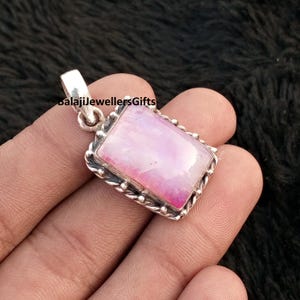 May include: A rectangular pendant with a pink and white stone set in a silver-colored metal frame. The frame has a beaded edge and a loop for a chain. The text "balajiJewellersGifts" is visible on the top left.