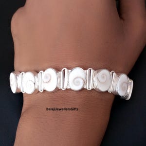 Peut inclure: Un bracelet en argent orné de segments blancs en forme de spirale. Les segments sont reliés par des maillons rectangulaires en argent. Le bracelet est présenté sur un poignet sur fond sombre. Le texte "BalajiJewellersGifts" est visible.