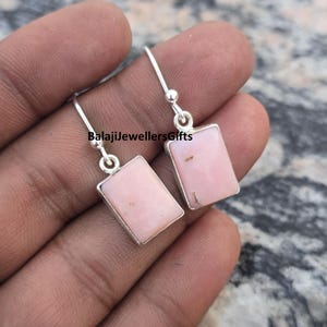May include: Silver earrings featuring rectangular, pale pink stones. The earrings have a simple design with a small ball at the top of the hook. The text "BalajiJewellersGifts" is visible.