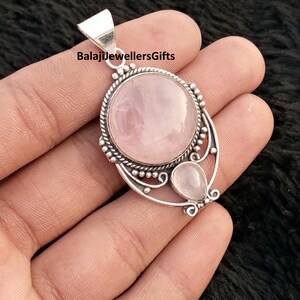 May include: A silver pendant with a large, round, pale pink rose quartz and a smaller, teardrop-shaped stone. The pendant has an intricate design, with the text "BalajiJewellersGifts" on the bail.