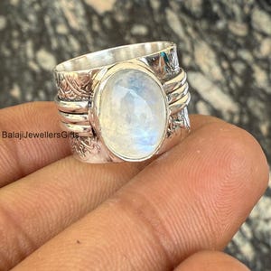May include: A silver ring with a large oval moonstone set in the center. The ring band is textured with a floral design.
