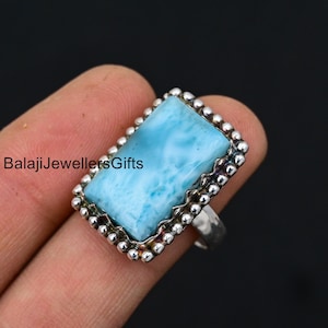 May include: A silver ring with a blue and white gemstone. The gemstone is set in a silver bezel with a beaded edge. The ring is on a finger.