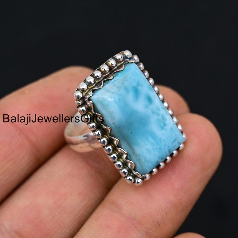 K&ouml;nnte beinhalten: Ein silberner Ring mit einem hellblauen Edelstein, der in einem Perlenrand gefasst ist. Der Edelstein hat eine wolkig-marmorierte Optik.