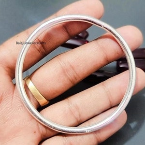 Op de afbeelding: Een zilveren armband, getoond op een hand, met een gladde, gepolijste afwerking.