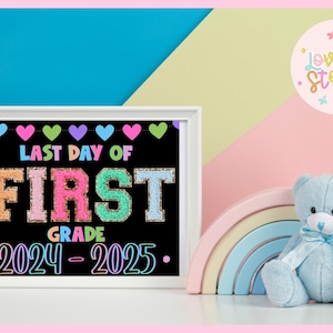 Könnte beinhalten: Ein weiß gerahmtes schwarzes Schild mit dem Text "Letzter Tag der ersten Klasse 2024-2025" in bunten Buchstaben. Die Buchstaben sind mit Glitzer und Herzen verziert.