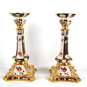 Puede incluir: Par de candelabros ornamentados. Los candelabros son blancos con detalles en negro y dorado. Las bases y los bordes son dorados. Están decorados con patrones florales rojos y blancos.