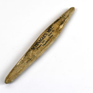 May include: A vintage wooden tool with a tapered shape, likely used for a specific craft or trade. The tool has a worn, aged appearance with visible wear and tear. The text "SCHINAGLE'S MKT." is printed on the side.