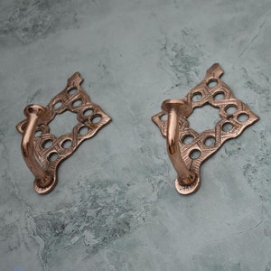 May include: Three ornate copper hooks with a diamond-shaped design. Each hook has a decorative, openwork pattern and a curved hook.