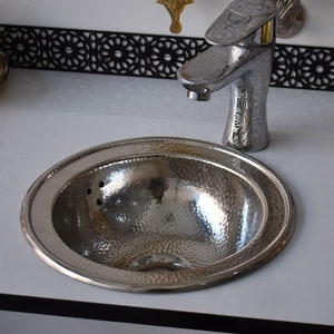 May include: A silver hammered metal sink with a round rim and a single faucet. The sink is set on a white countertop.