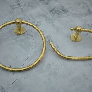 May include: Two gold-toned towel rings with a textured finish. The larger ring is circular, while the smaller ring is oval shaped.