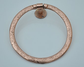 May include: A copper towel ring with an ornate design. The ring is circular and has a decorative pattern of leaves and vines.