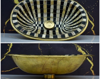 May include: An oval brass sink with a black and white chequered pattern. The sink has a brass drain stopper.