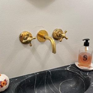 May include: A black marble bathroom sink with a white pumpkin decoration, gold faucet, and a clear glass bottle with a pink liquid and a gold pump dispenser.