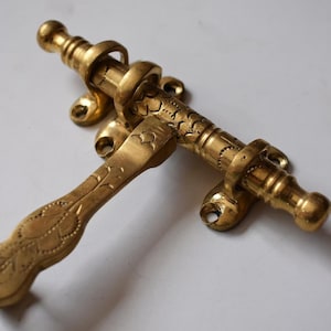 以下が含まれることがあります： 装飾的なデザインの真鍮製のドアボルト。ボルトにはレバーハンドルと装飾的なノブが付いています。