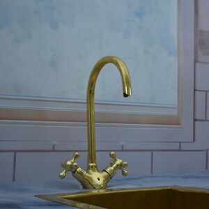 May include: A gold-toned kitchen faucet with two handles and a curved spout. The faucet is mounted on a white countertop.
