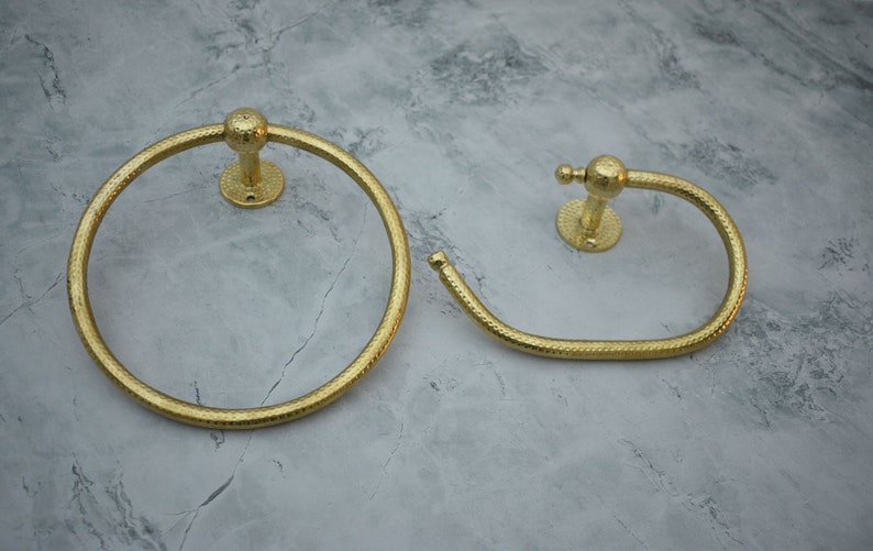 May include: Two gold-toned towel rings with a textured finish. The larger ring is circular, while the smaller ring is oval shaped.