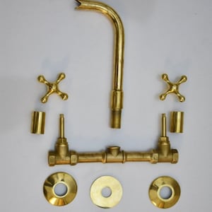 May include: Brass bathroom faucet set with two handles, a spout, and three round escutcheons. The faucet is disassembled and laid out on a white surface.