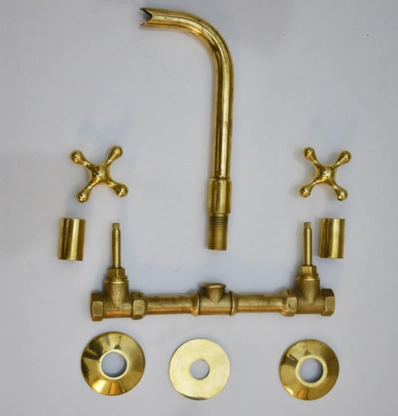 May include: Brass bathroom faucet set with two handles, a spout, and three round escutcheons. The faucet is disassembled and laid out on a white surface.