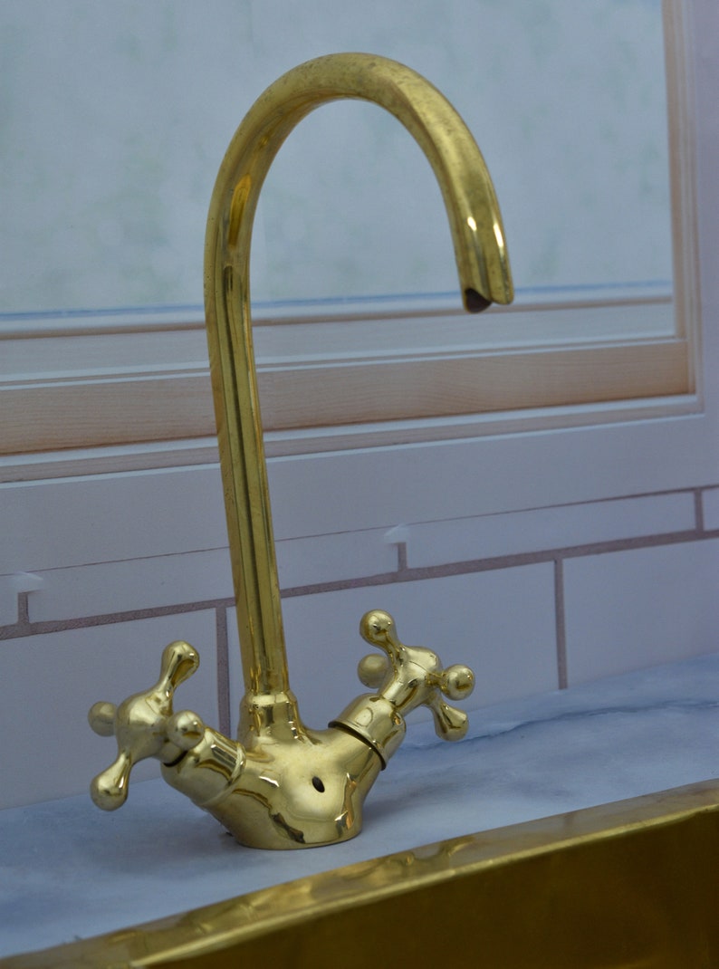 May include: A gold-toned faucet with two cross-shaped handles. The faucet has a curved spout and is mounted on a countertop.