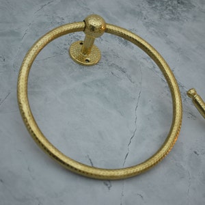 May include: Two gold-toned towel rings with a hammered finish. The rings are mounted on a wall.