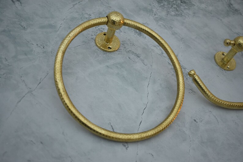 May include: Two gold-toned towel rings with a hammered finish. The rings are mounted on a wall.