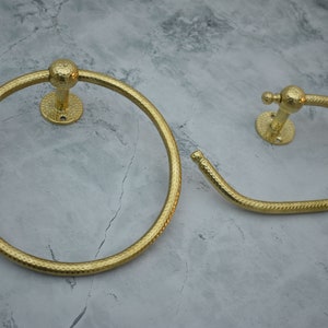 May include: Two gold-toned towel rings with a hammered finish. The larger ring is circular, while the smaller ring is a curved shape.