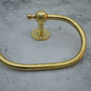 May include: Gold-toned hammered metal towel ring with a round base and a decorative knob.