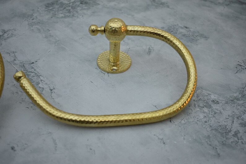 May include: Gold-toned hammered metal towel ring with a round base and a decorative knob.