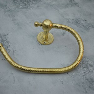 May include: Two gold-toned metal towel rings with a hammered texture. The rings are attached to a wall with a round base.