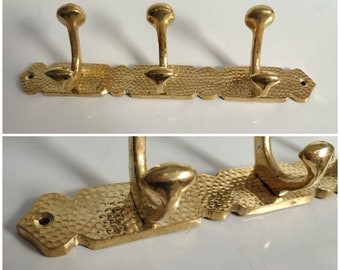 May include: A gold-toned metal coat rack with three hooks. The rack has a textured surface and a decorative design.