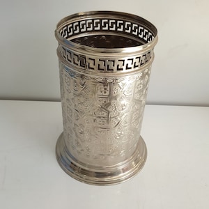 Puede incluir: Paraguas de metal plateado con un diseño ornamentado. El soporte tiene una forma cilíndrica con una parte superior e inferior decorativas.
