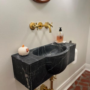 May include: A black marble vessel sink with a gold faucet and a small white pumpkin with orange accents on the counter.