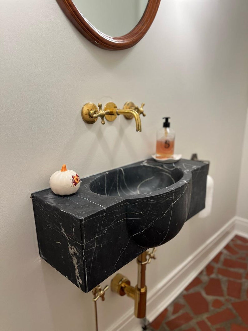 May include: A black marble vessel sink with a gold faucet and a small white pumpkin with orange accents on the counter.