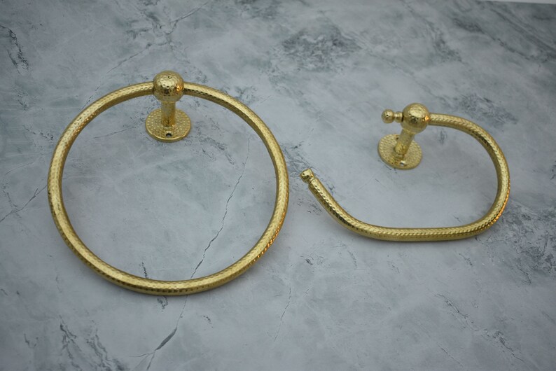 May include: Two gold-toned towel rings with a textured finish. The rings are mounted on a wall.
