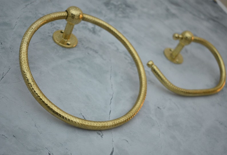 May include: Two gold-toned towel rings with a hammered finish. The rings are mounted on a wall.