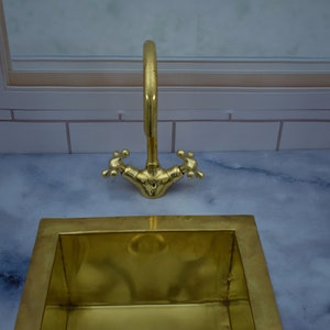 May include: A gold-toned sink with a matching faucet. The sink is rectangular and has a smooth, polished surface. The faucet has a single handle and a spout that curves upwards.