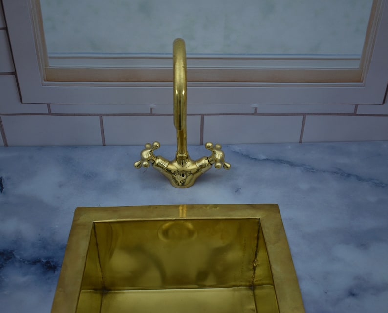 May include: A gold-toned sink with a matching faucet. The sink is rectangular and has a smooth, polished surface. The faucet has a single handle and a spout that curves upwards.