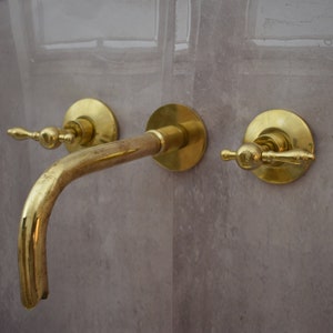 May include: A gold-toned bathroom faucet with two handles and a curved spout.