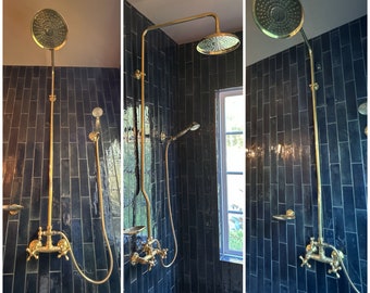 May include: A gold shower head with a long arm and a handheld shower head. The shower is installed in a bathroom with dark blue subway tiles.