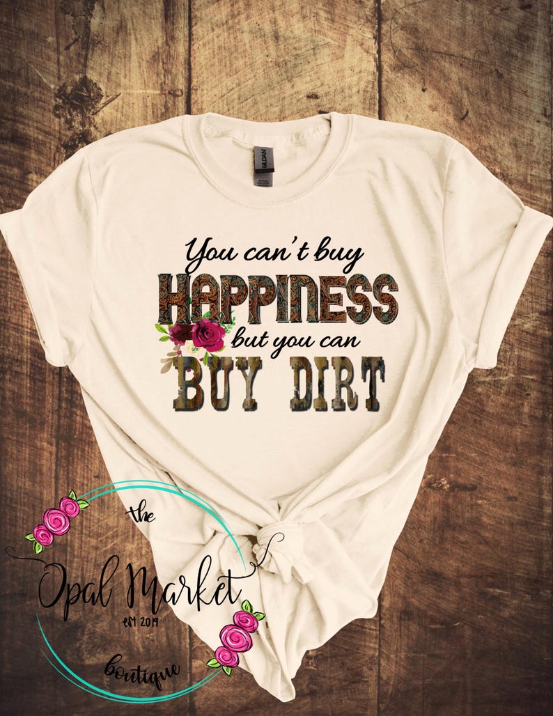 May include: A white t-shirt with the text "You can't buy happiness but you can buy dirt" printed on it. The text is in a brown and black camouflage pattern with pink flowers.