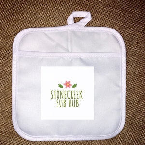 May include: White square pot holder with a pocket and a hanging loop. The pot holder features the text "STONECREEK SUB HUB" in green with a pink flower and green leaves.