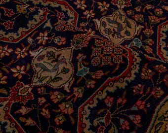 May include: Close-up of a Persian rug with a detailed floral and bird pattern. The rug features a navy blue background with red, beige, and green accents. The intricate design includes stylized flowers and birds, creating a rich, textured appearance.