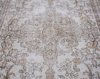 May include: A vintage rug with a beige background and a brown floral pattern. The rug has a distressed look, with some areas faded and worn.