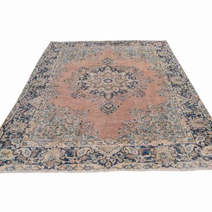 May include: A large, rectangular rug with an intricate floral pattern. The rug features a central field in a muted rose color, surrounded by a border of navy blue and cream. The design includes detailed floral and geometric motifs.